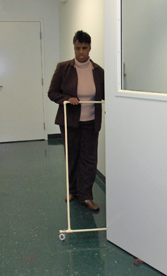 Three photos show the woman approaching the same door edge she approached in the first photos, trailing the wall with her left hand and pushing the AMD ahead of her with her right hand.  When the AMD reaches the edge of the door, it stops while the woman is still a few feet away from the door.